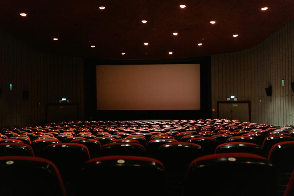 A dimly lit empty cinema theater with rows of red chairs facing a projector screen.
